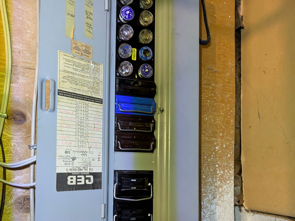 An older fuse panel with its cover open, showing screw-in plug fuses, cartridge fuse pull-outs and a handwritten circuit directory.
