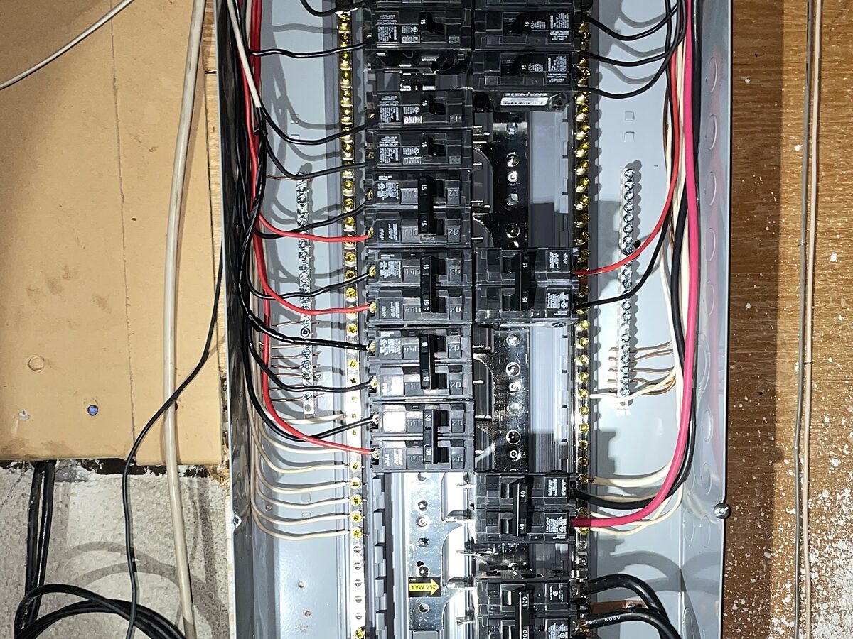 A breaker panel with its cover removed, showing branch circuit conductors routed to the breakers and terminated at the neutral bars.