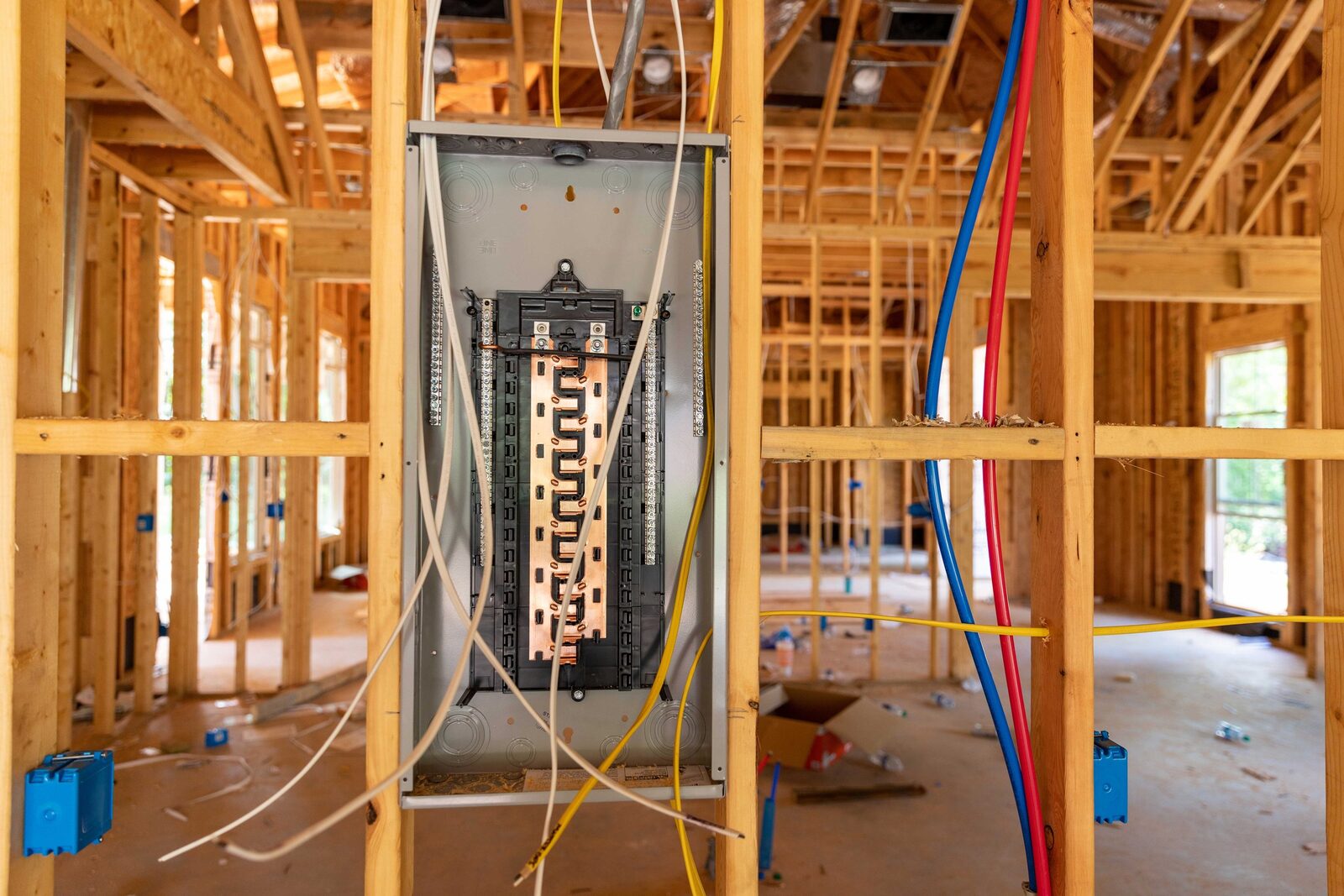 Rough-in wiring running through the open wooden stud framing of a house under construction, with cables landing at a panel enclosure before the walls are closed.