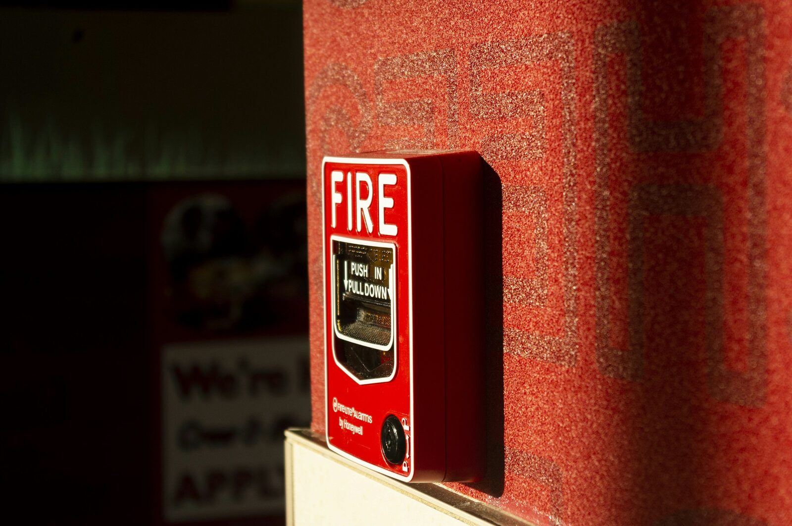 A red fire alarm pull station mounted on a textured red wall.
