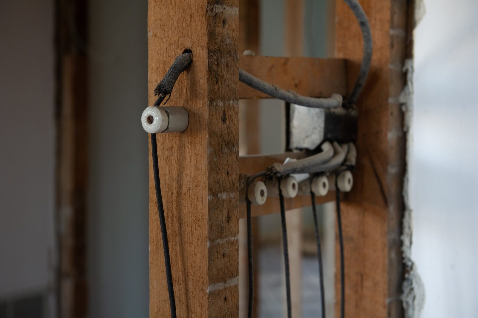 Knob and tube wiring exposed in an open stud wall: single cloth-covered conductors supported clear of the timber on white ceramic knobs, running down from an older metal junction box.