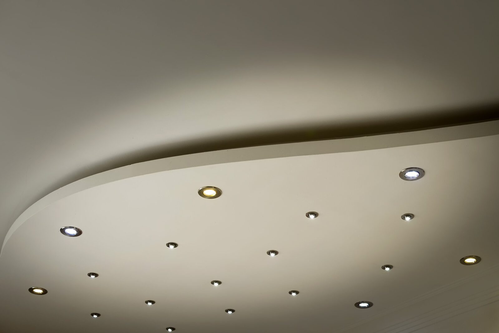 A curved stepped ceiling fitted with rows of small recessed downlights, several of them lit and others switched off.
